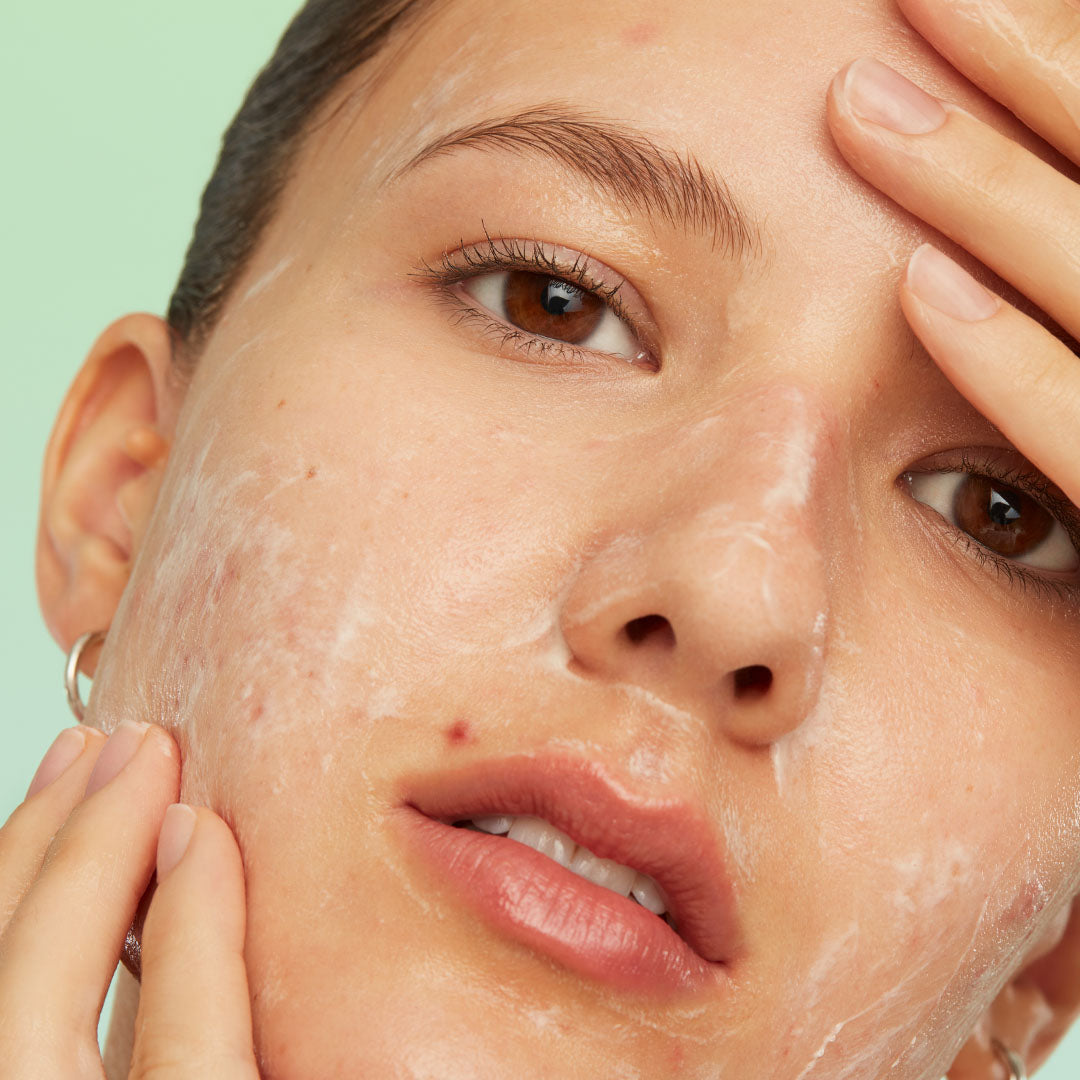 A woman gently cleanses her sensitive skin with CUSHION CLEANSE, lather visible on her face.