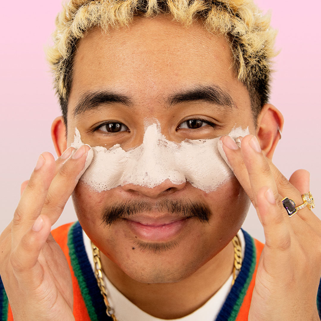 Smiling person applies PORE VAC Clearing Clay Mask, set against a pink gradient background.