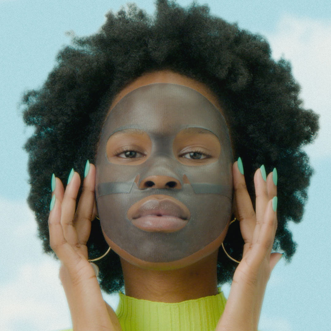 A woman applies PRESS REFRESH exfoliating sheet mask for acne-prone skin; sky-blue background.