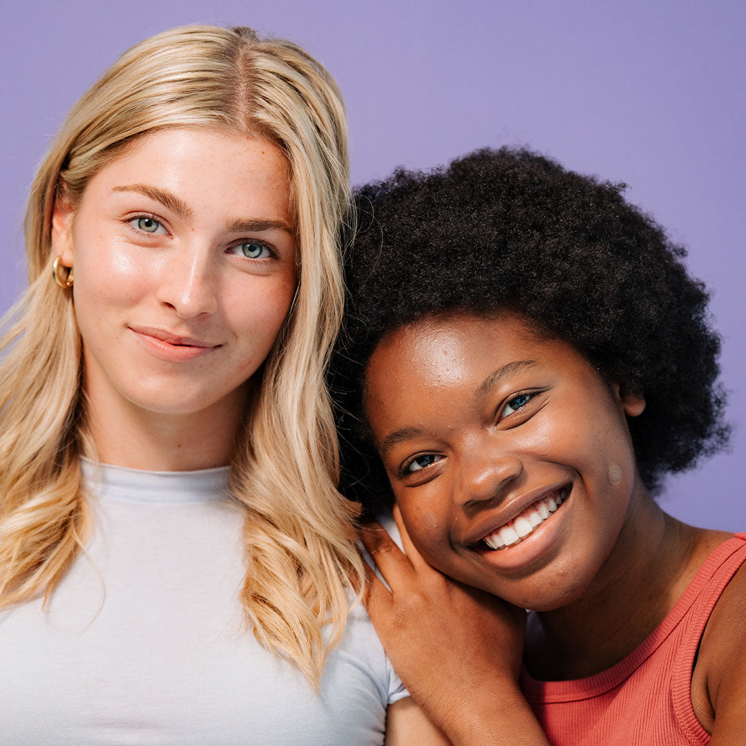 Two young women smile in front of purple, showing off UNDERCOVER Blemish Patches Quarterly 3 Pack Bundle.