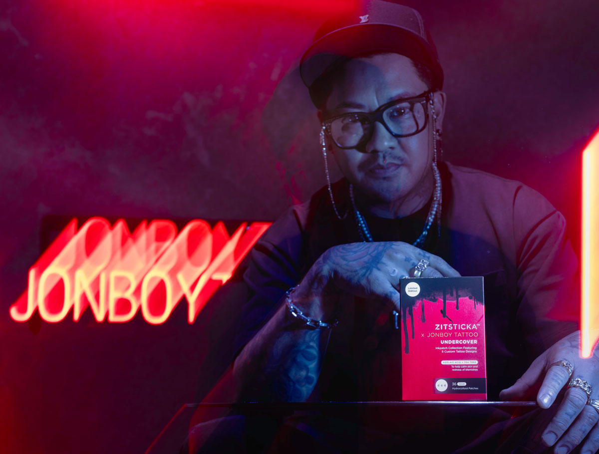 A person in glasses and a cap holds the Zit Glam Pack with neon JONBOY text glowing behind them.
