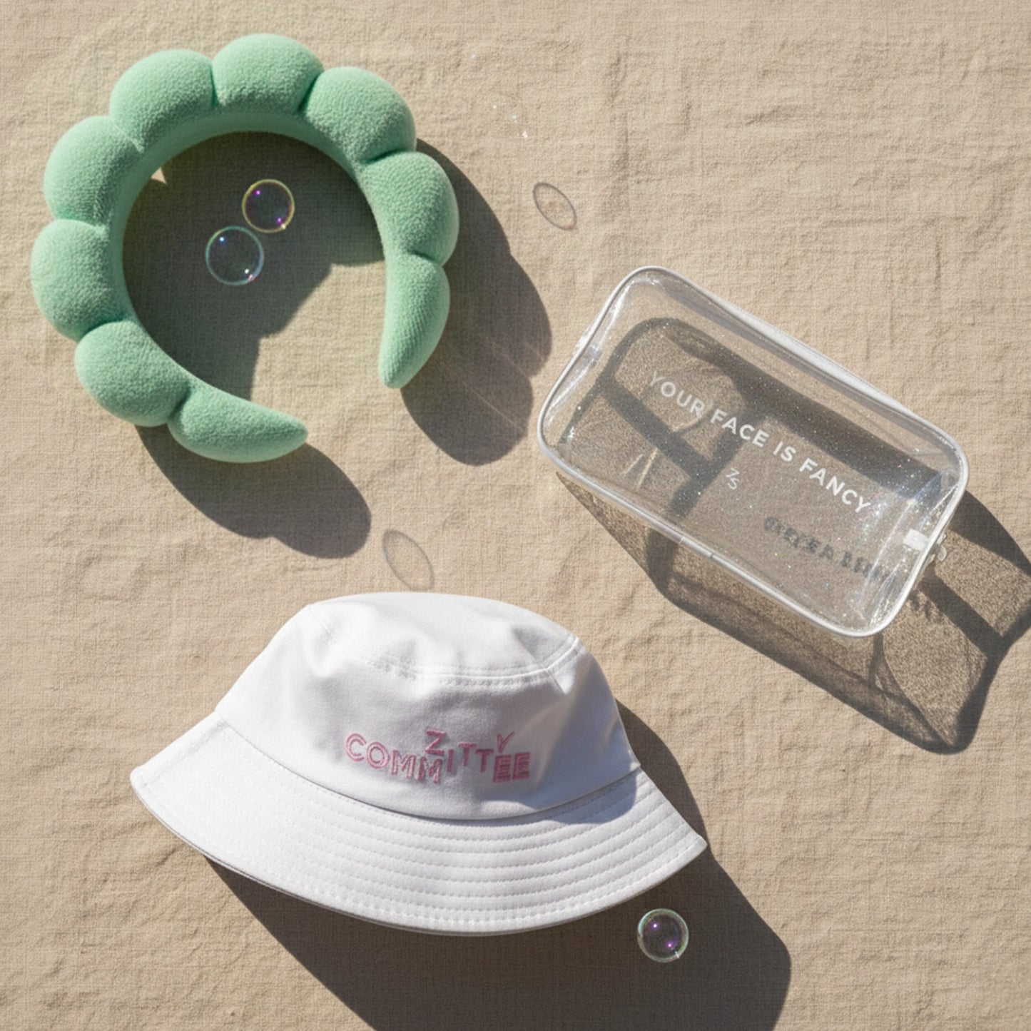 #ZittyCommittee Kit: green headband, glitter make-up bag & white bucket hat in sunlight with bubbles.