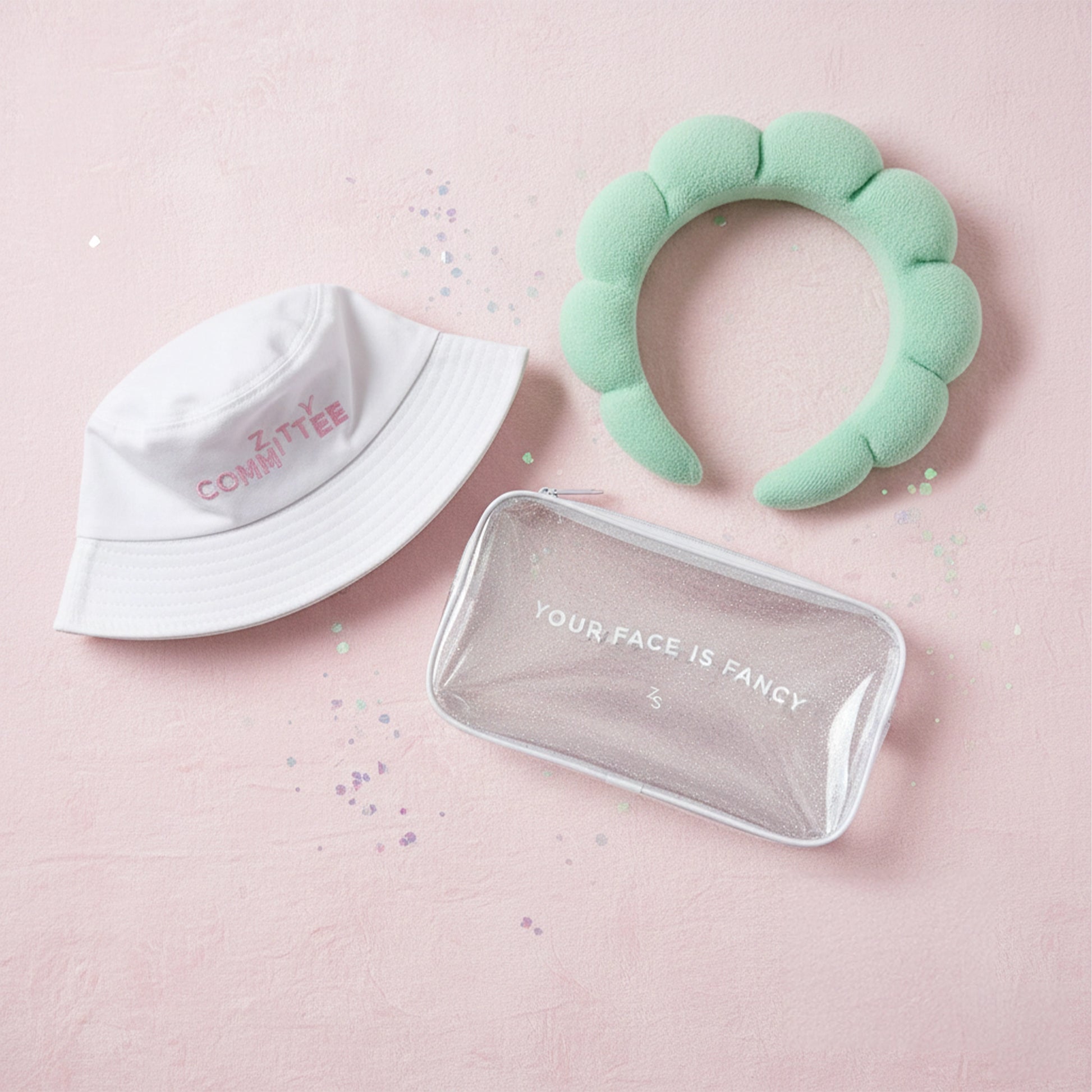 #ZittyCommittee Kit with white bucket hat, mint green headband, and glitter bag on a pink sparkly surface.